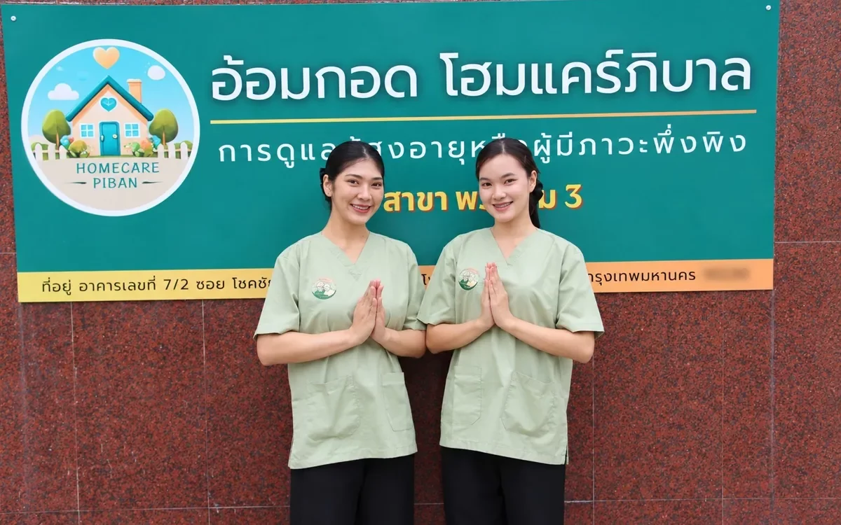 ทีมผู้ดูแลในชุดสครับสีเขียวยกมือไหว้หน้าป้ายอ้อมกอด โฮมแคร์ภิบาล สาขาพระราม 3 ยานนาวา กรุงเทพฯ