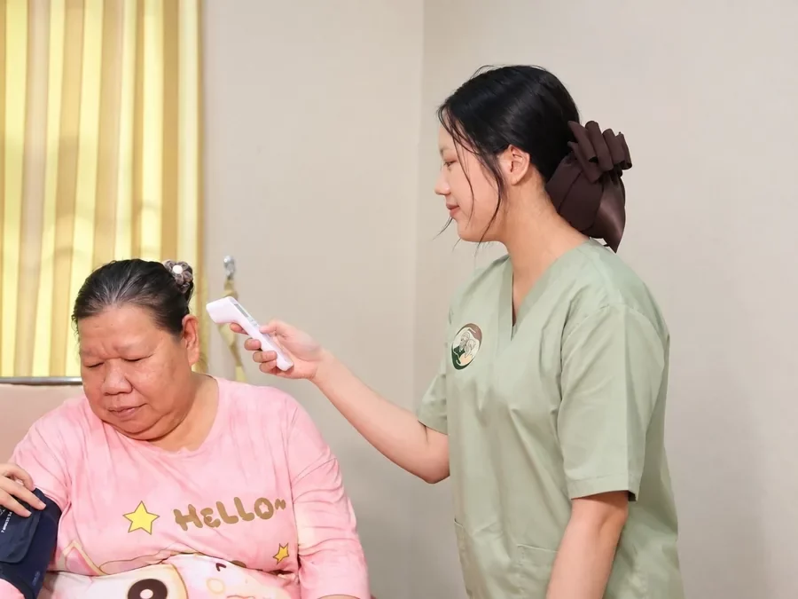 ผู้ดูแลวัดอุณหภูมิร่างกายให้คุณยายด้วยเครื่องวัดไข้ทางหน้าผาก