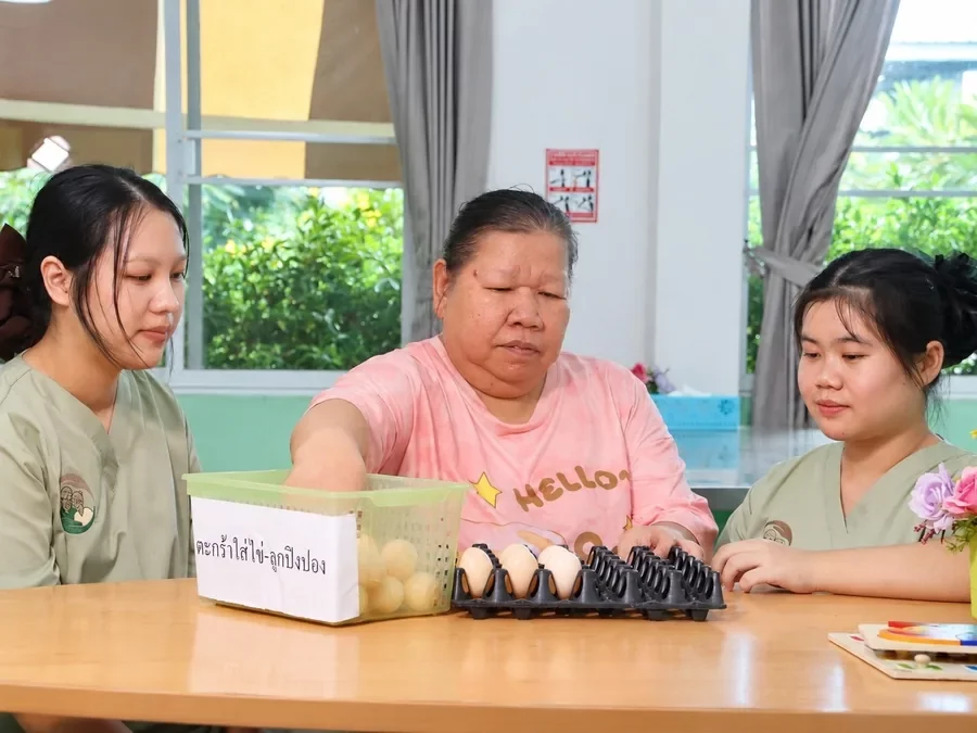 คุณยายหยิบไข่และลูกปิงปองใส่แผง ฝึกมือและสมาธิ กับผู้ดูแล 2 คน