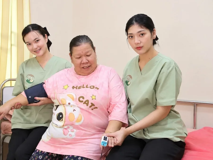 ผู้ดูแลวัดความดันและค่าออกซิเจนปลายนิ้วให้คุณยายบนเตียง